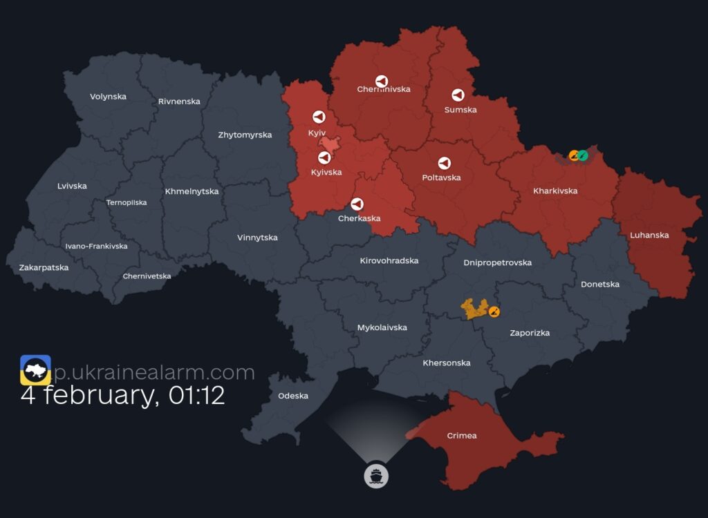 En karta över Ukraina från flyglarmsappen visar ett pågående flyganfall natten den 4 februari klockan 01:12. De områden som är markerade i rött indikerar regioner under flyglarm, vilket inkluderar Kyiv och flera omkringliggande regioner, såsom Chernihivska, Sumska, Poltavska och Kyivska. Piktogram i form av varningstrianglar och ikoner för hotande drönare eller missiler syns över de drabbade regionerna. Den visuella kontrasten mellan de röda och grå områdena på kartan förstärker allvaret i situationen, där röda zoner symboliserar akut fara. De gråa områdena, där inget flyglarm är aktivt, förstärker känslan av hur selektivt och utbrett hotet kan vara. I nedre vänstra hörnet visas appens logotyp och en tidsangivelse som understryker att detta är en realtidsuppdatering av situationen. Kartan fångar en del av den verklighet som invånarna i Ukraina dagligen lever med – en ständig vaksamhet mot luftangrepp.